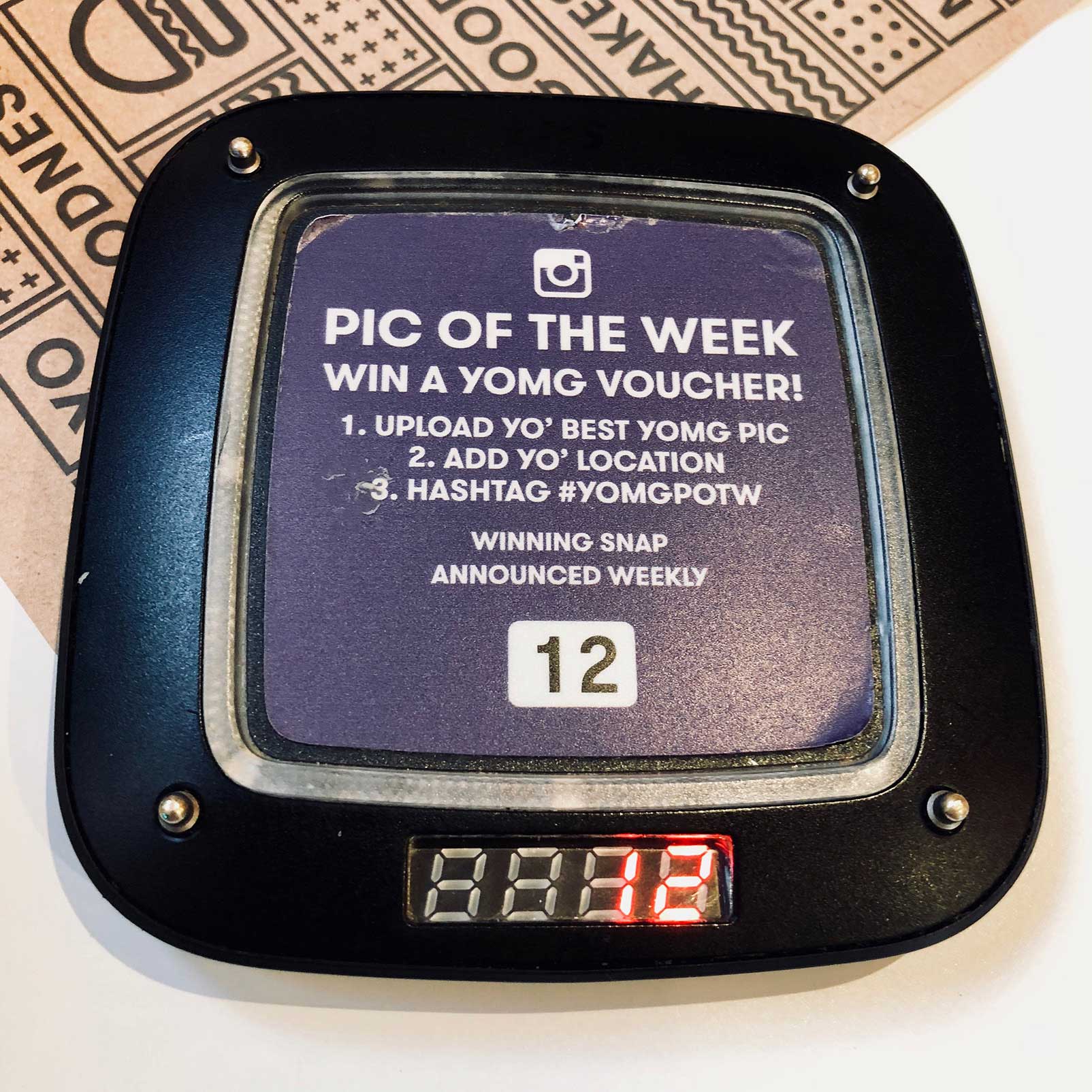 YOMG's photo contest prompt on a coaster-shaped restaurant buzzer